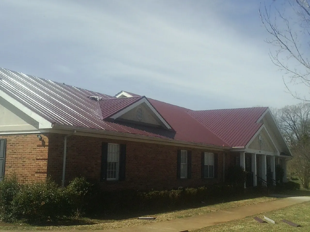Red metal roof with gabled entries on a long brick building, from a Hail Damage Roof Repair job in Layton