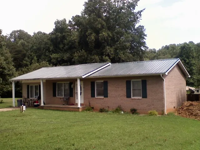 Gray metal roof on a brick ranch house with a side carport in Layton