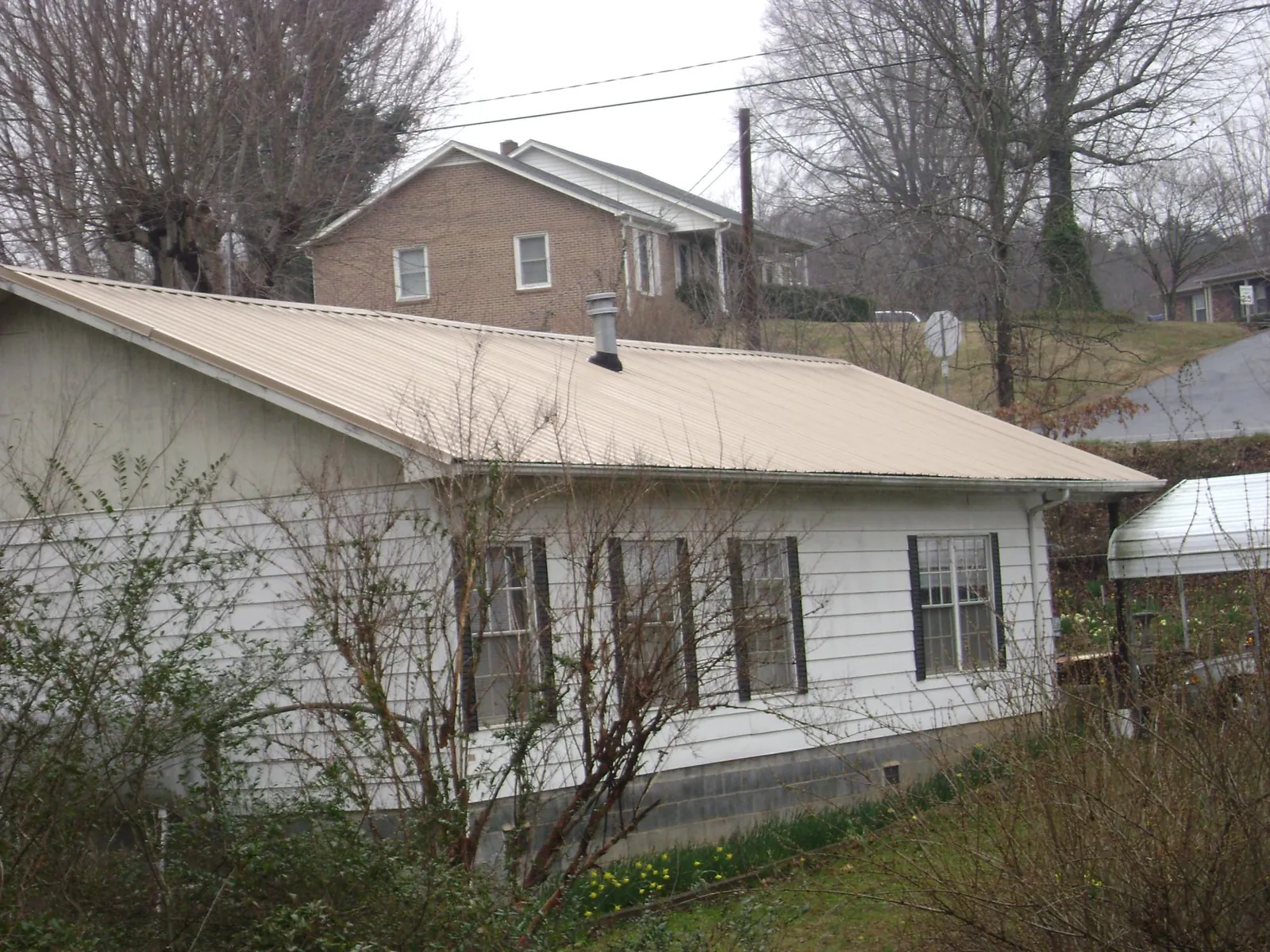 Tan metal roof on a white sided house set into a hillside — Commercial Roofing by Roofing Brothers in Layton