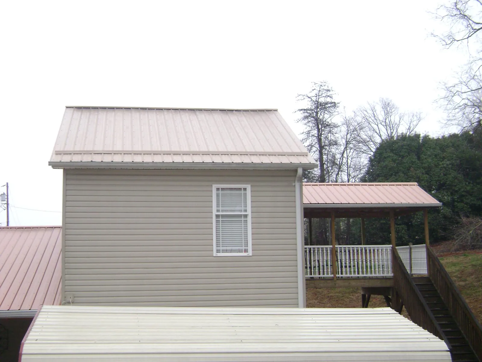 Tan metal roofs on a two story addition and attached porch, from a Roof Replacement job in Layton